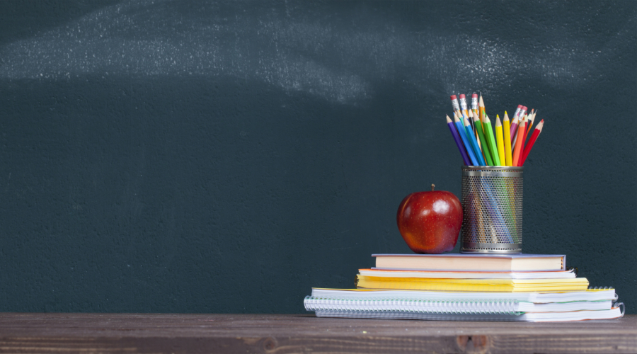 Pencil tray and an apple on notebooks on school teacher’s desk.