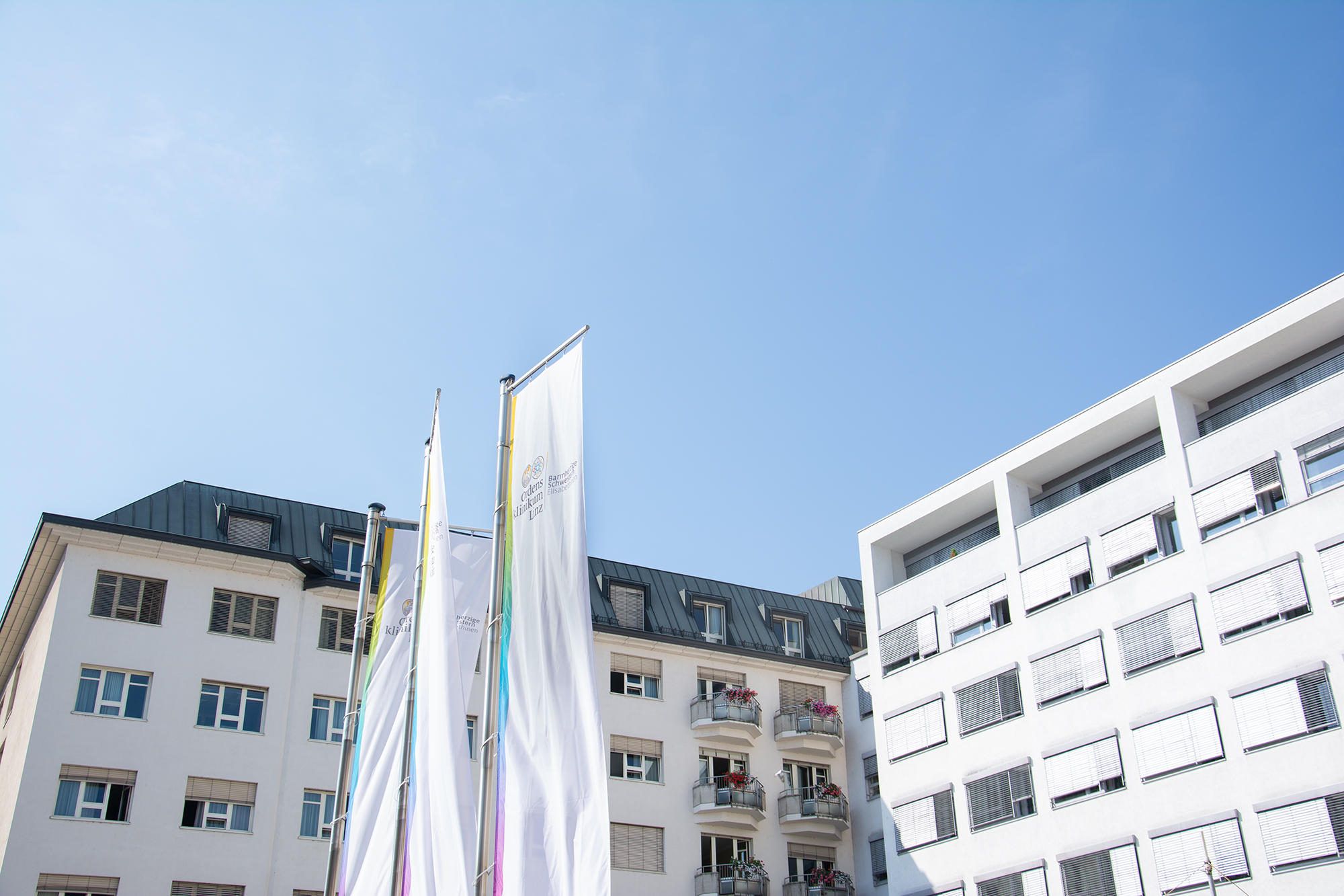 Das Krankenhaus BHS Linz ist von außen zu sehen, darüber strahlend blauer Himmel.