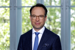 Porträt von Prof. Dr. Christoph Arnoldner. Ein Mann Mitte 40 mit dunklem Haar und Brille. Er trägt einen Anzug mit blauer Krawatte und lächelt in die Kamera.