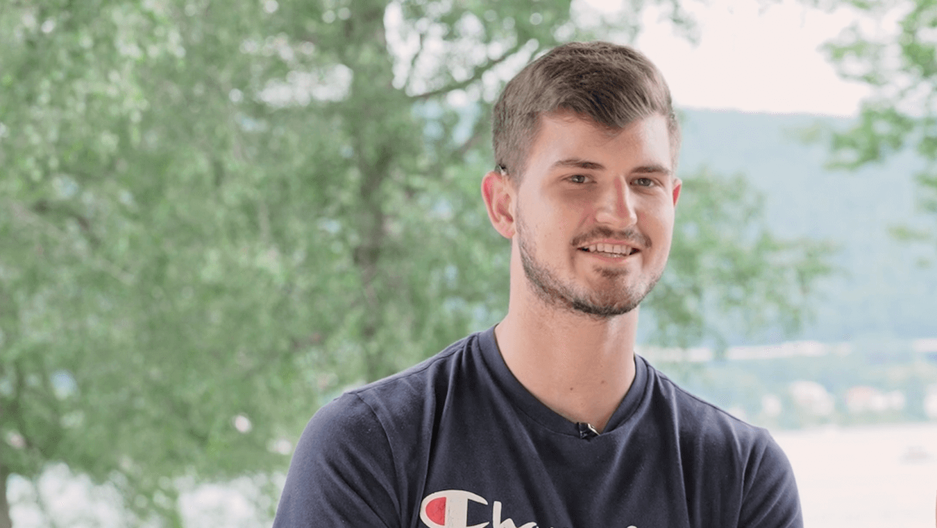 Porträt von Matthias Pusker: ein junger Mann Anfang 20. Er hat brauenes Haar und einen kurzen Bart. Lächelt in die Kamera, trägt ein dunkelblaues Shirt.