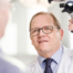 Foto von Prim. Dr. Thomas Keintzel. Ein Mann in den 40ern mit Brille und blondem Haar. Er ist dabei einen Patienten zu untersuchen und schaut deshalb nicht direkt in die Kamera.